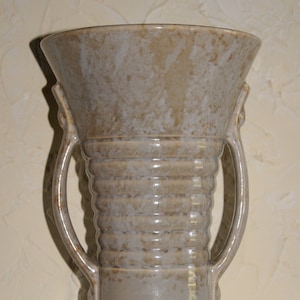May include: A ceramic vase with two handles, a light brown glaze, and a ribbed design.