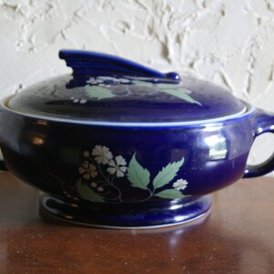 May include: A cobalt blue ceramic serving dish with a lid. The dish has a floral design in white and green. The lid has a handle on top.