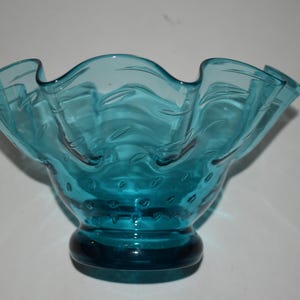May include: A teal blue glass bowl with a ruffled rim and a textured bottom. The bowl is made of clear glass with a blue tint.