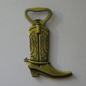 May include: A metallic gold-colored bottle opener shaped like a cowboy boot. The boot features decorative stitching, a spur, and a heel. The top of the boot is designed as a bottle opener.
