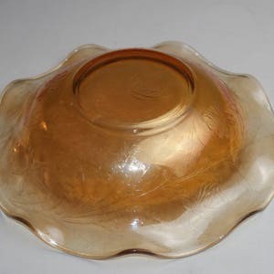 May include: A vintage amber glass bowl with a scalloped edge and a floral pattern. The bowl is made of iridescent glass and has a shiny finish.