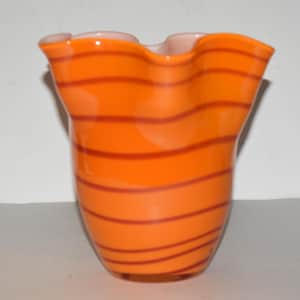 May include: Orange and pink glass vase with a wavy, ruffled rim and a striped pattern.