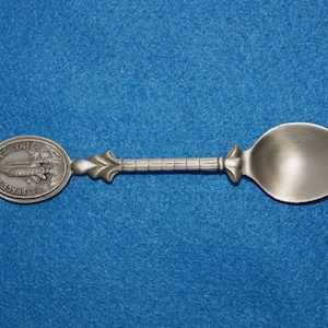 May include: A silver spoon with a round, engraved handle featuring the text "U.S. Space & Rocket Center".