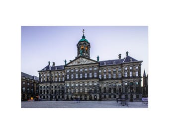 Op de afbeelding: Het Koninklijk Paleis van Amsterdam is een groot, meerverdiepings stenen gebouw met een centrale koepel, een klokkentoren en talloze rechthoekige ramen. Het bouwwerk heeft een fronton met gedetailleerd beeldhouwwerk en een groen koperen dak.