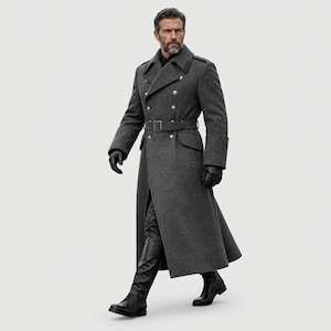 May include: A charcoal gray double-breasted wool overcoat featuring a wide notched lapel, silver-toned buttons, and a matching waist belt with a rectangular buckle. The long coat is worn with black leather gloves, black trousers, and boots.
