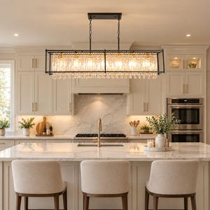 May include: A rectangular kitchen island chandelier featuring a matte black metal frame and multiple vertical clear glass crystal prisms. The light fixture is suspended by two thin chains and illuminates a kitchen space with warm light.