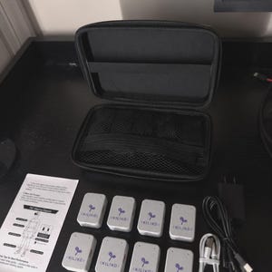 May include: A black zipped carrying case with an internal mesh pocket, eight white rectangular motion tracking sensors labelled KILIKO with a purple sprout logo, a white USB charging cable, a black power adapter, and an instruction manual.