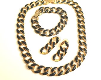 May include: A gold-toned jewelry set featuring a necklace, bracelet, and earrings. The chain-link design has black enamel accents. The set is displayed on a white background, showcasing the contrast between the gold and black.