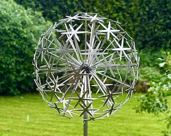 May include: A spherical garden sculpture made of silver-colored metal, featuring a dandelion-like design with numerous star-shaped wire elements radiating from a central point, mounted on a thin, straight vertical metal rod stake.