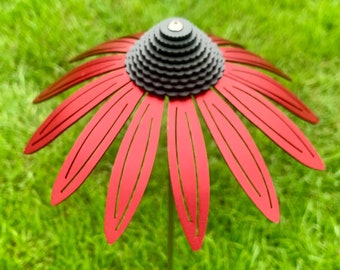 May include: Red metal flower with a black center, standing in a green grassy lawn.