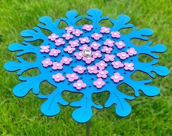 May include: A blue metal garden stake with a circular design featuring pink flowers. The stake is designed to look like a stylized flower.
