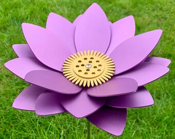 May include: A purple metal flower with a gold center, standing in a grassy area.
