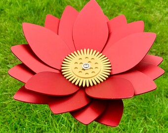 May include: A red metal flower with a gold center, standing in a green grassy area.