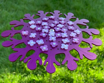 May include: Purple metal flower with a decorative design and small white flowers attached. The flower is on a metal stake.