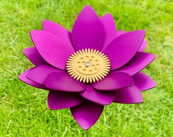 May include: A purple metal flower with a yellow center, standing in a green grassy area.