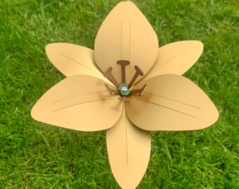 May include: A papercraft flower with six petals in a light yellow color. The flower has a green center with a small, clear gem in the middle.