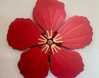 May include: A red metal hibiscus flower wall decor with a gold center. The flower has five petals and is a popular tropical design.