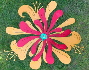 May include: A metal flower wind spinner with yellow and pink petals. The flower has a green center with a swirl design.