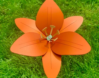 May include: A large, orange paper flower with six petals. The flower is made of paper and has a gold center.