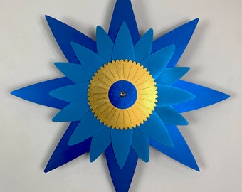 May include: A blue and gold paper starburst with a layered design. The center of the starburst is a gold circle with a blue center.