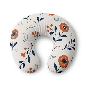 Könnte beinhalten: Ein U-förmiges Stillkissen mit cremefarbenem Hintergrund und einem wiederkehrenden Muster aus orangefarbenen Blumen, dunkelblauen Blättern und kleinen Beerenclustern. Das Design enthält zudem dünne, geschwungene dunkelblaue Linien.