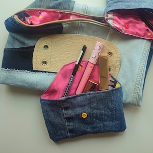 May include: Three denim pouches with pink satin lining. The largest pouch has a leather flap with two eyelets. The pouches are filled with makeup and sunglasses.