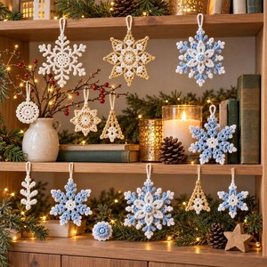 May include: A collection of crocheted ornaments in white, gold, and light blue, featuring snowflake, star, and tree shapes. These decorative items are suspended by loops and displayed alongside a white vase, a candle, and pine branches.