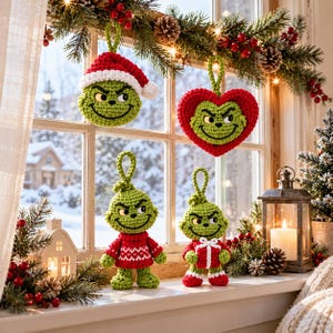 May include: Four handmade crochet ornaments featuring a green character with a mischievous expression. Two are hanging decorations, one wearing a red and white Santa hat and one shaped like a red heart. Two are standing figures in red sweaters.