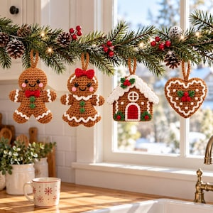 Pode incluir: Quatro enfeites de Natal de crochê pendurados em uma guirlanda de pinheiro: um boneco de gengibre com gravata borboleta vermelha, um com laço vermelho, uma casa de gengibre com porta vermelha e um biscoito em forma de coração com bagas.