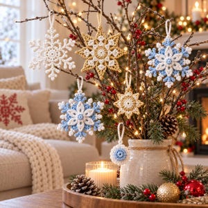 May include: A collection of six crocheted snowflake ornaments in white, gold, and light blue hanging from bare branches in a ceramic vase. The ornaments feature intricate geometric patterns and loops for hanging, displayed with pinecones and red berries.
