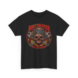 Peut inclure: Un t-shirt noir avec une impression graphique représentant un crâne portant un bandana, placé devant deux clés à molette croisées. Le motif inclut des flammes rouges et jaunes, avec le texte BUILT FOR SPEED et HIGH PERFORMANCE.