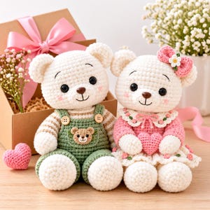 Puede incluir: Dos osos de peluche tejidos a ganchillo. El oso de la izquierda lleva un peto verde con un pequeño parche de oso y una camisa a rayas. El oso de la derecha lleva un vestido rosa con cuello floral, un corazón rosa y un lazo rosa con flor.