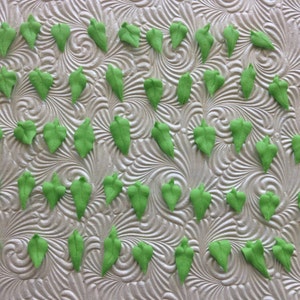 May include: A collection of 40 green fondant leaves, perfect for decorating cakes and cupcakes. The leaves are arranged in rows on a white surface.