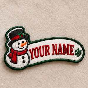 May include: An embroidered patch featuring a snowman wearing a black top hat with a red band and a red scarf. The snowman has an orange carrot nose. To the right, a white banner with a dark green border displays the red text YOUR NAME.