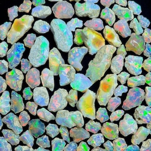May include: A collection of raw, unpolished opal stones featuring a milky white base with vibrant flashes of green, blue, orange, and pink colour play. Each stone has an irregular, natural shape with rough, textured edges.