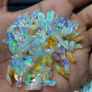 May include: A collection of small, irregular, translucent opal gemstones featuring a vibrant play-of-color with flashes of neon green, electric blue, and warm orange hues. These polished, multi-faceted stones exhibit a milky white base.