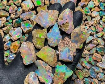 May include: A collection of raw, unpolished opal stones featuring a natural, rough texture and a vibrant play-of-color. The stones display iridescent flashes of green, blue, orange, and pink against a milky, translucent, and earthy base.