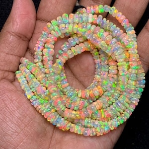 May include: A strand of small, round, translucent opal beads featuring a vibrant play-of-color with flashes of neon green, orange, yellow, and pink throughout the surface of each individual gemstone bead arranged in a circular pattern.