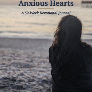 May include: A book cover titled Peace for Anxious Hearts: A 52-Week Devotional Journal. The cover features a dark-haired individual viewed from behind, sitting on a sandy beach at sunset, with the text NewCreationsSupply at the bottom.