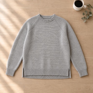May include: A light gray long-sleeve sweater featuring a crew neckline, raglan sleeves, and a ribbed hem with side slits. The knit garment has a consistent texture throughout the body and sleeves, providing a clean and simple appearance.