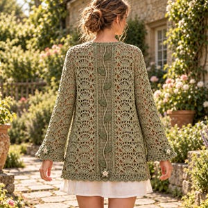 May include: A sage green crochet cardigan featuring an intricate fan stitch pattern, long sleeves with floral accents at the cuffs, and a central vertical panel decorated with a vine motif and small leaves, worn over a white skirt.