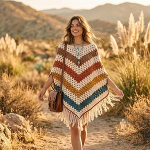 May include: A crochet poncho featuring a chevron pattern in cream, brown, orange, yellow, and teal, finished with long fringe along the bottom hem. The garment is worn with a brown leather crossbody bag and a layered silver necklace with blue stones.