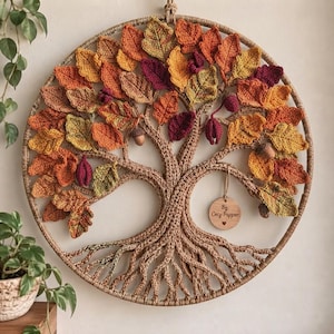 May include: A circular wall hanging featuring a crocheted tree with intricate roots and branches. The tree is adorned with numerous crocheted leaves in shades of orange, yellow, red, and brown, along with small acorns. A wooden tag reads By Cecy Papper.