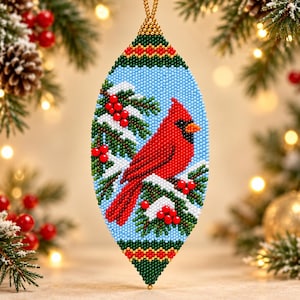 May include: A teardrop-shaped beaded ornament featuring a bright red cardinal bird perched on a snowy pine branch with red berries against a light blue background. The top and bottom edges are decorated with green and gold bead patterns.