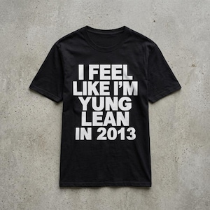 May include: A black short-sleeved t-shirt featuring bold white text centred on the chest that reads I FEEL LIKE I'M YUNG LEAN IN 2013. The garment has a standard crew neckline and a straight hemline, presented in a flat, front-facing view.