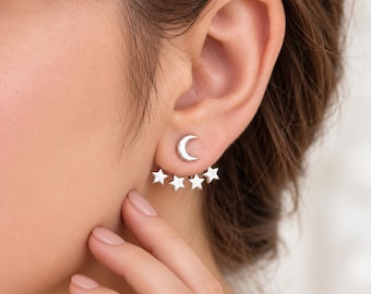 May include: A silver-toned ear jacket earring featuring a crescent moon stud that sits on the earlobe, with a detachable curved bar attachment underneath that displays four small, evenly spaced five-pointed stars.