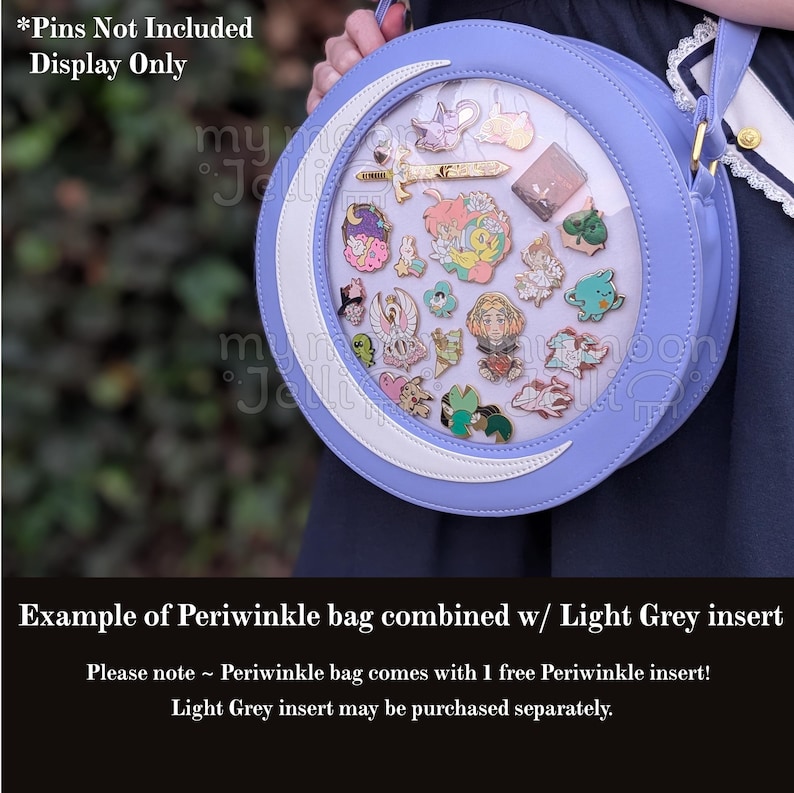 May include: A periwinkle blue round bag with a white crescent moon design and a clear plastic window. The bag is filled with enamel pins. The text "*Pins Not Included Display Only" is visible at the top of the image. The text "Example of Periwinkle bag combined w/ Light Grey insert" is visible at the bottom of the image. The text "Please note ~ Periwinkle bag comes with 1 free Periwinkle insert! Light Grey insert may be purchased separately." is also visible at the bottom of the image.