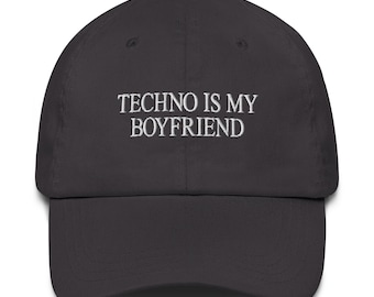 May include: A dark gray baseball cap with the embroidered text "TECHNO IS MY BOYFRIEND" in white. The cap has a curved brim and a rounded crown, suitable for casual wear. The hat is made of a soft fabric.