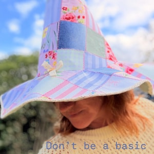 May include: A patchwork witch hat featuring various pastel fabric squares in light blue, pink, and floral patterns with a white lace trim along the brim and a small white bow accent. The text "Don't be a basic witch....." is visible on the image.