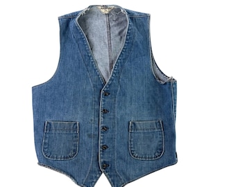 Könnte beinhalten: Eine mittelblaue Jeansweste mit V-Ausschnitt, fünf dunklen Knöpfen an der Vorderseite und zwei aufgesetzten Taschen an der Taille. Das Kleidungsstück hat einen ausgefransten Rand am Ausschnitt und an den Ärmelausschnitten sowie einen spitzen Saum.